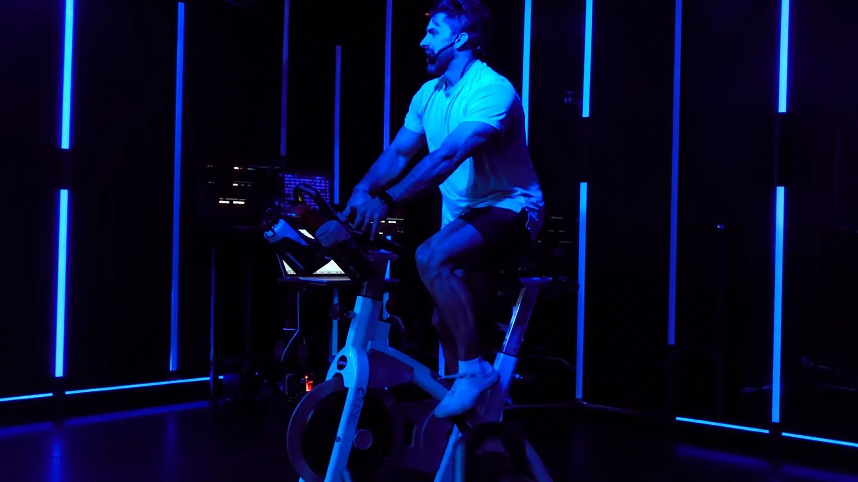 Professional spin instructor leading an indoor cycling class with blue LED lighting.