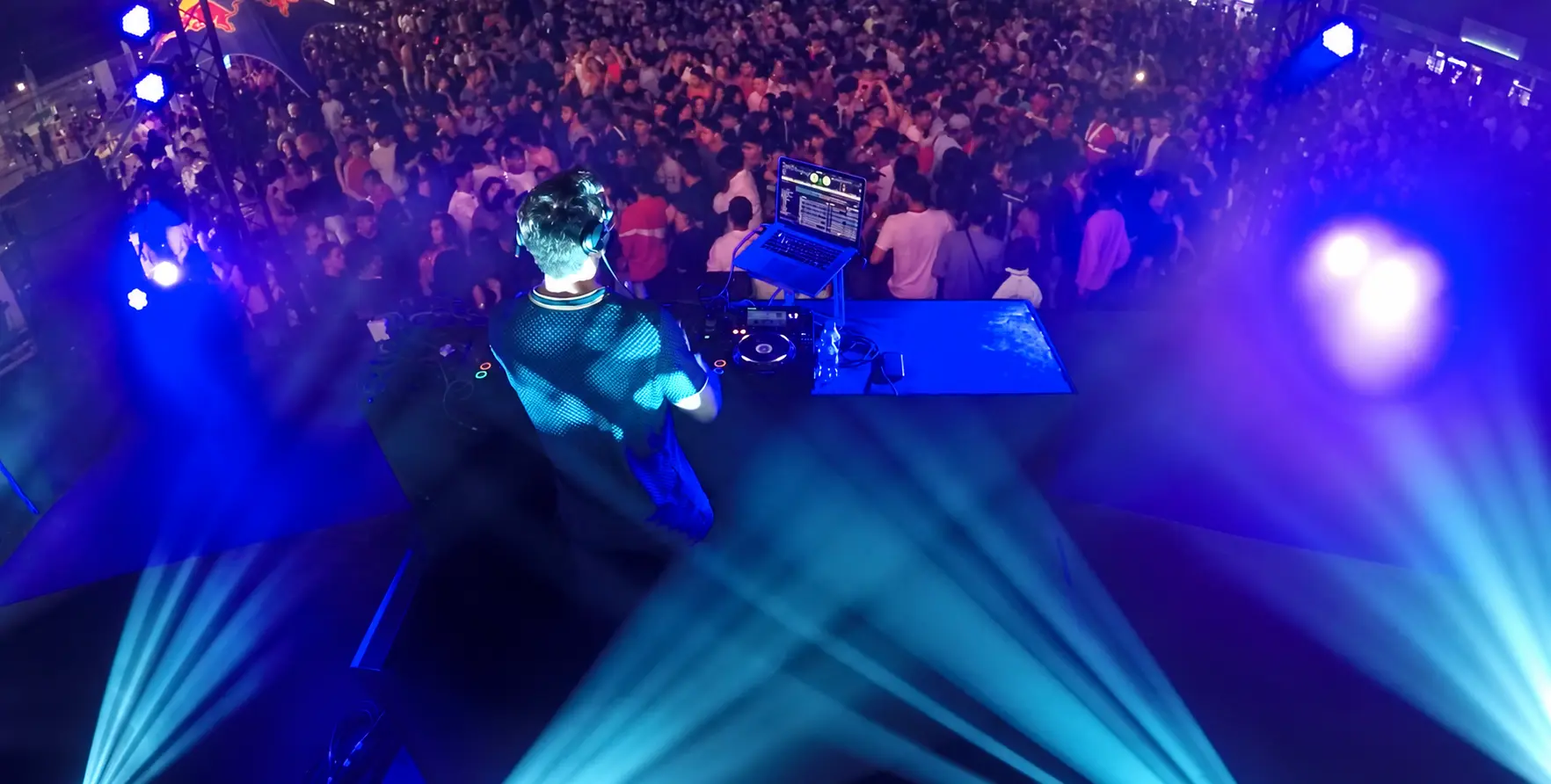 Darryl Rees behind the DJ decks at du Arena in Abu Dhabi, facing a large crowd under blue and purple stage lighting.
