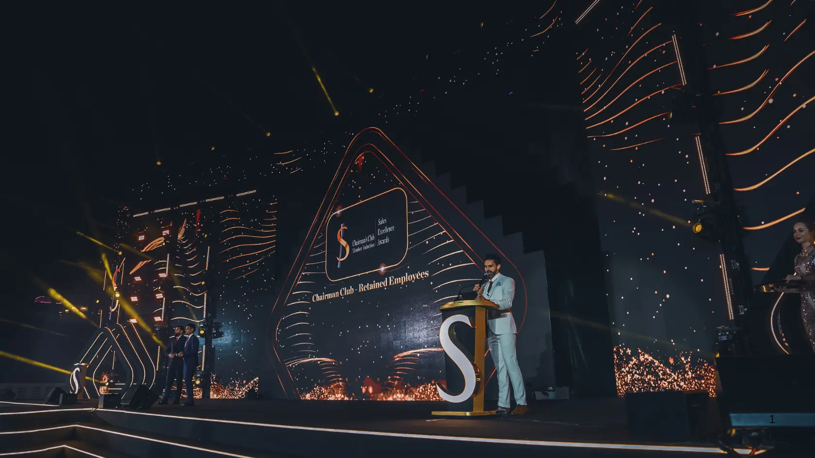 Darryl Rees speaking into a microphone at a gold podium on the illuminated Sobha Realty Awards stage.