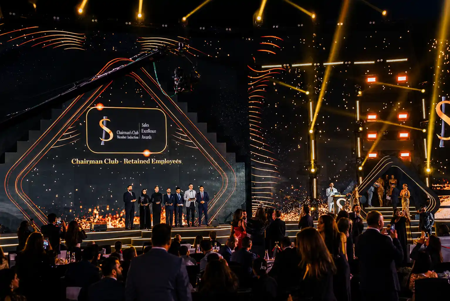 Professional event MC presenting a corporate awards ceremony in Dubai with immersive LED staging, dramatic lighting effects, and a packed audience.
