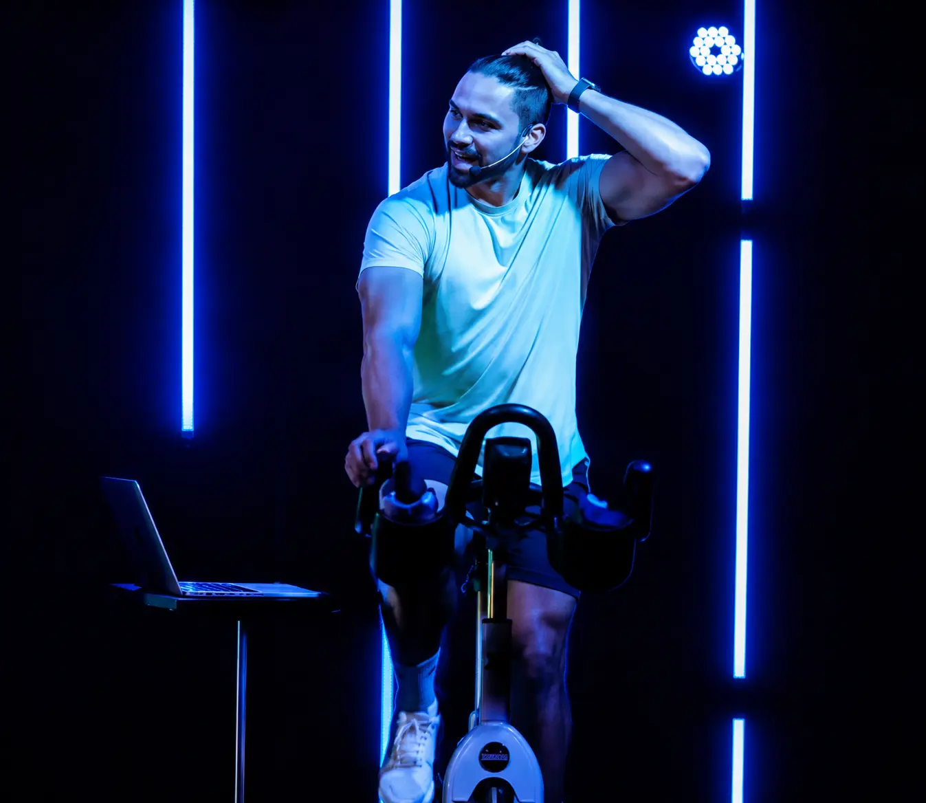 Professional spin instructor leading an indoor cycling class with blue LED lighting.