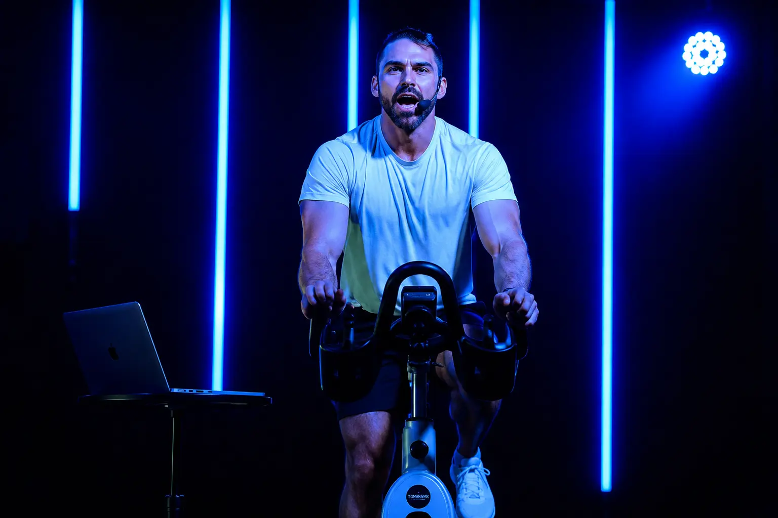 Dubai spin instructor leading a high-energy indoor cycling class in a modern fitness studio with blue LED lighting.