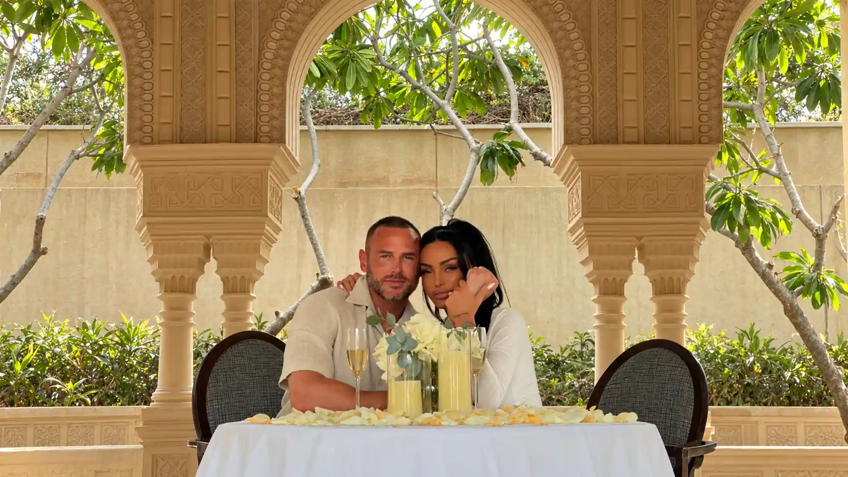 Katie Price and Lee Andrews seated together at a flower-decorated table beneath an ornate stone arch in Dubai.