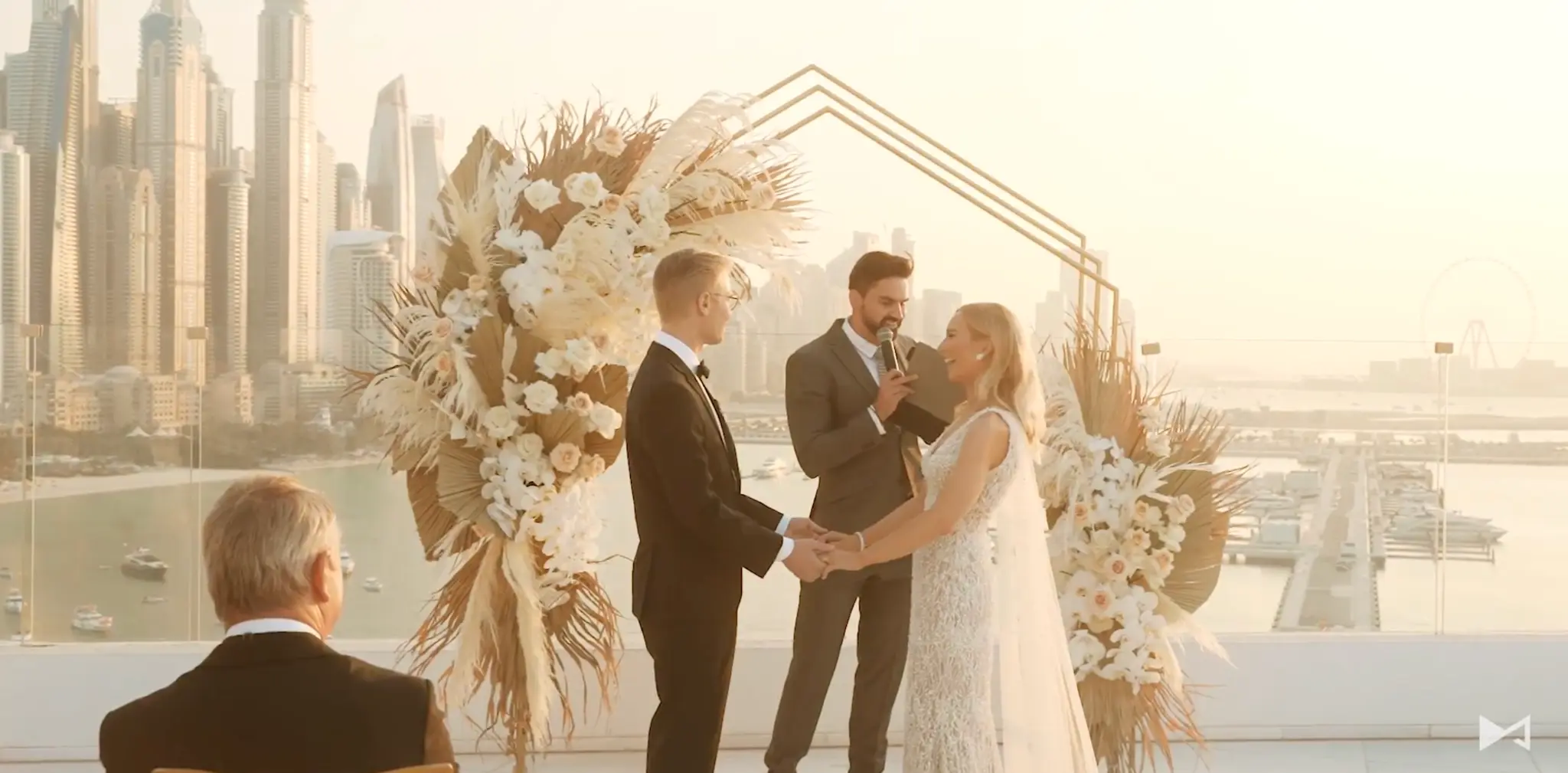 Wedding celebrant Darryl Rees conducting Victoria and Wes’ outdoor ceremony in Dubai, framed by elegant floral arrangements and the city skyline at sunset.
