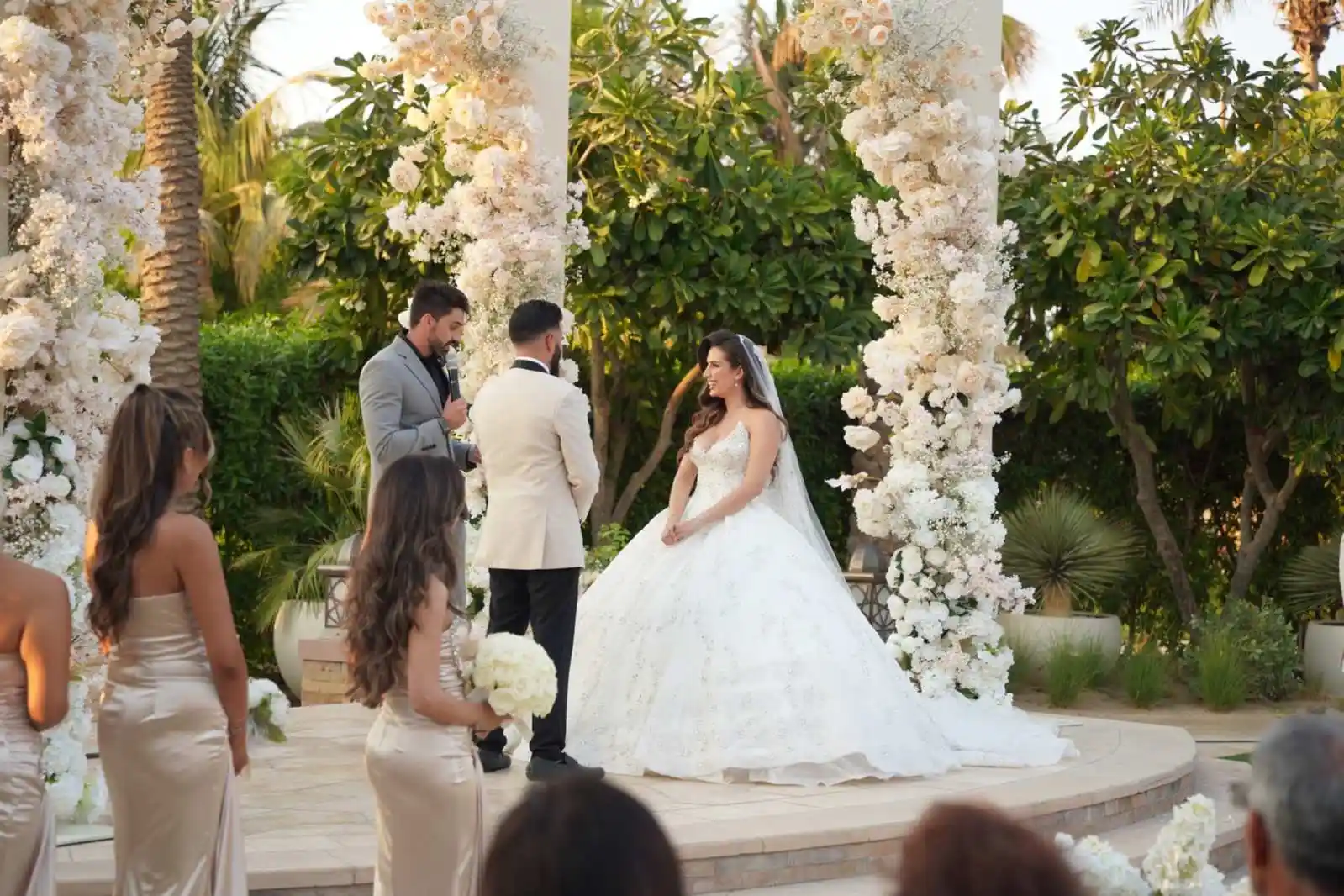Wedding celebrant Darryl Rees leading Sevim and Kaya’s outdoor ceremony, with white floral arrangements and bridesmaids watching nearby.
